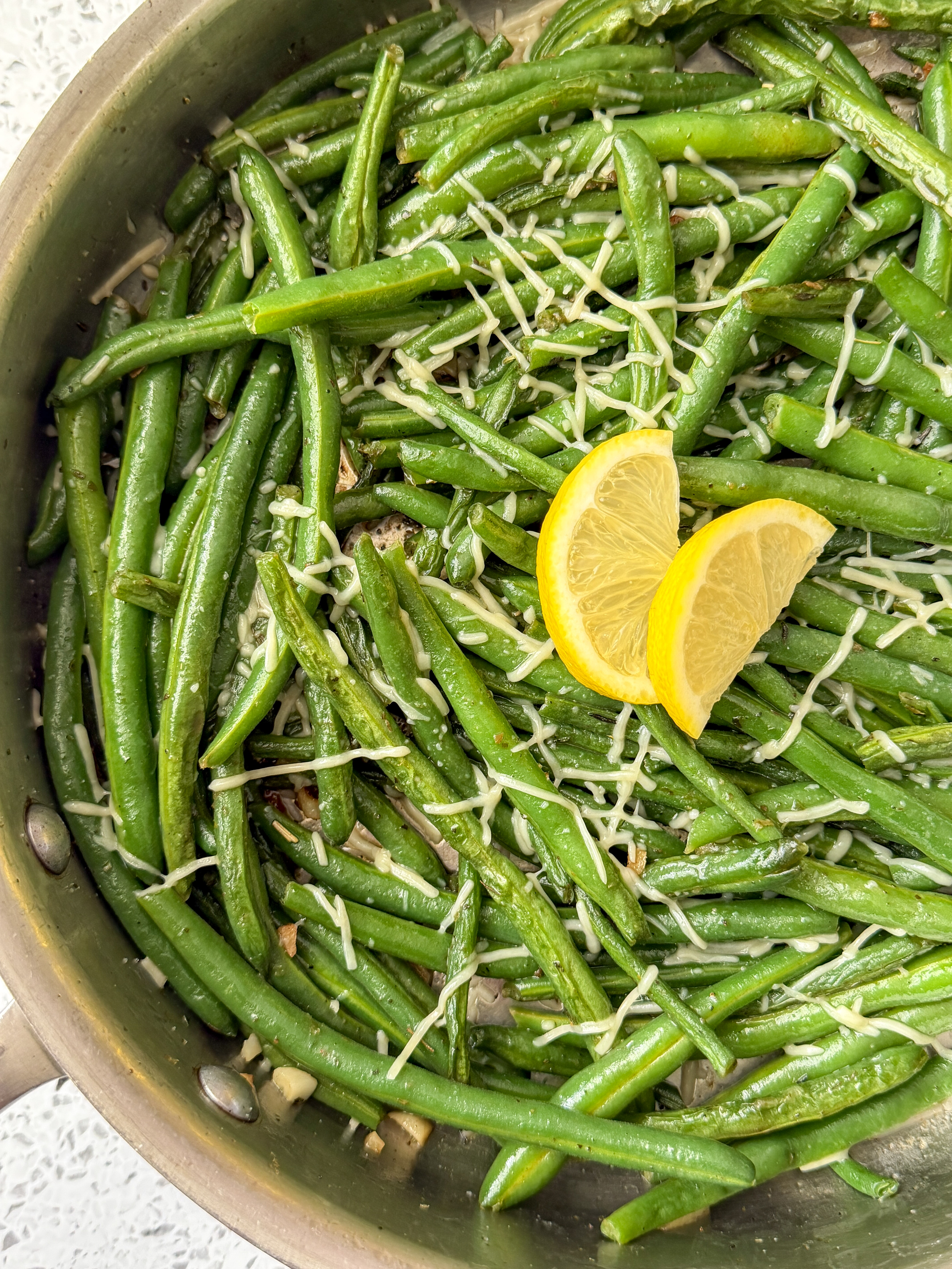 Garlic green beans sautéed with fresh garlic and Parmesan cheese, garnished with lemon slices.
