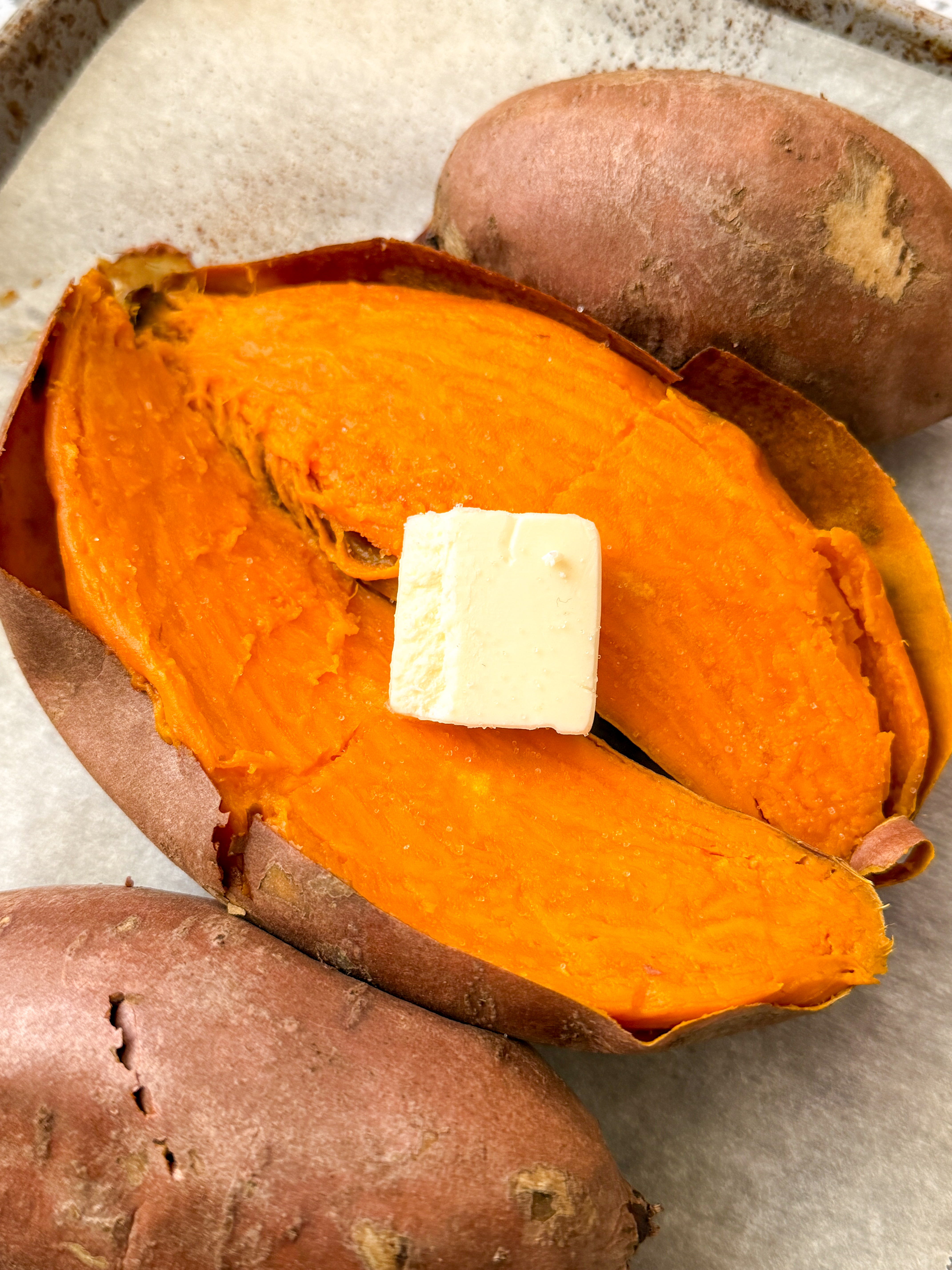 Freshly baked sweet potato split open with a pat of butter melting on top.